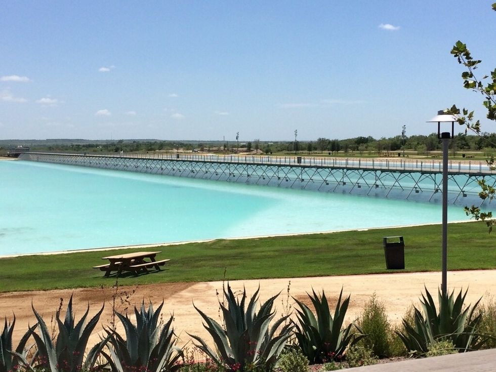Pristine turquoise lagoon, picnic table, agave plants, and bridge under a clear sky, NLand surf park