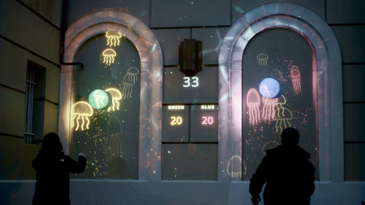 Projected jellyfish game on building wall, two people interacting, scores displayed.