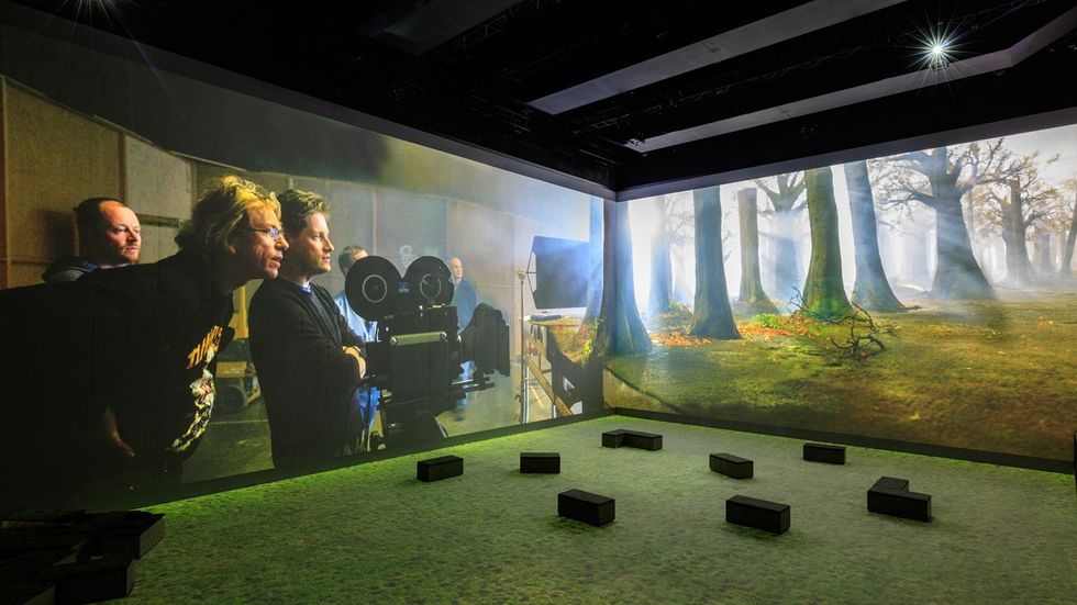 Projection of filmmakers and forest scene in a modern, immersive exhibit space.