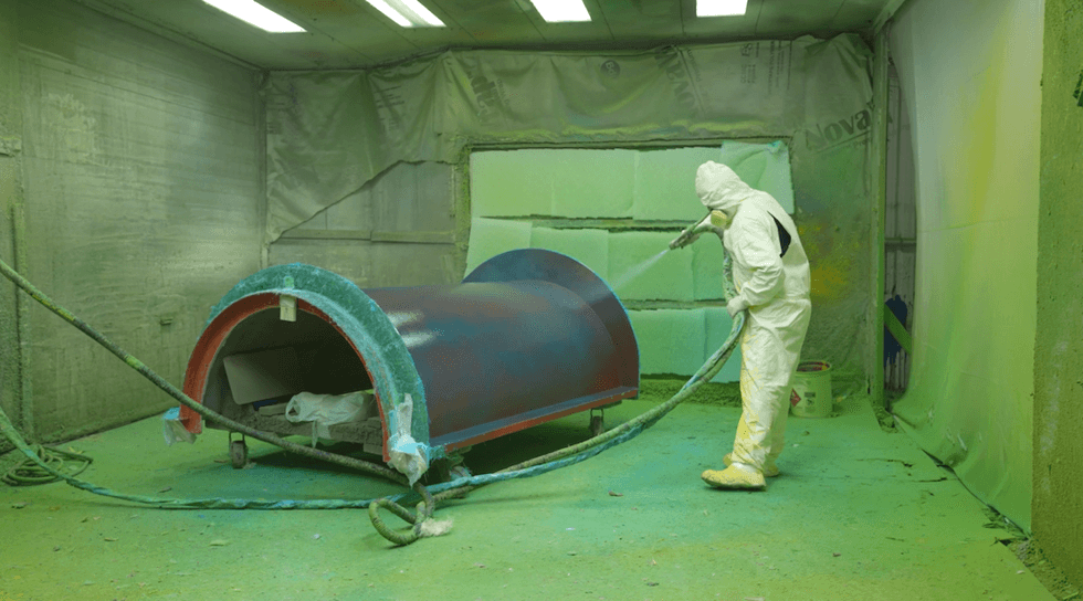 ProSlide worker in protective gear spray-painting a water ride section in an industrial booth.