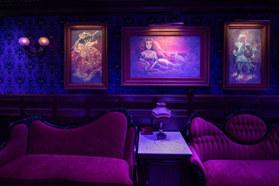 Purple-lit room with ornate couches and three illuminated paintings on a patterned wall.