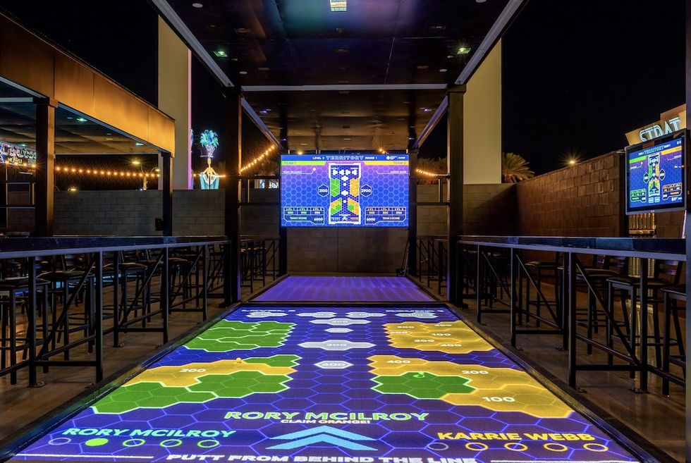 Putting District indoor digital golf course with colorful hexagonal patterns and electronic screens.