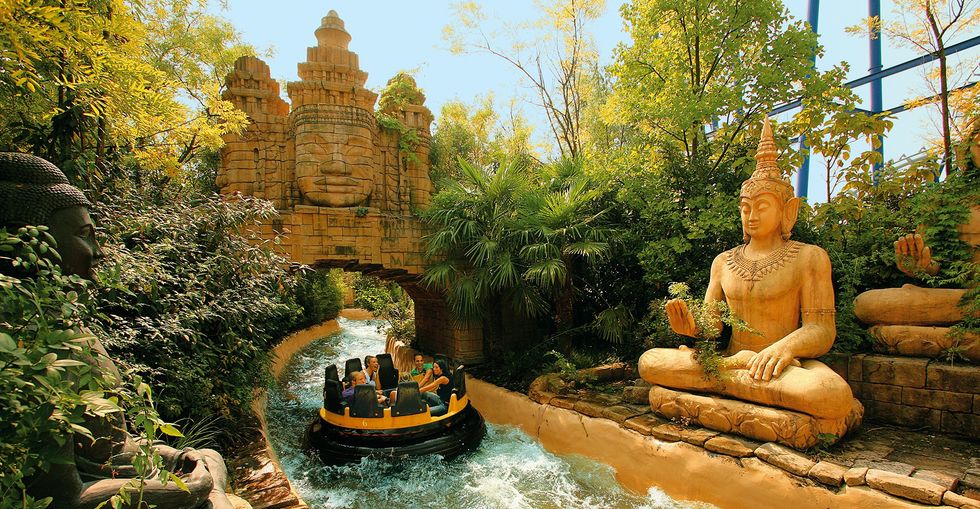 Rafting ride at Gardaland through lush greenery and ancient temple ruins with large seated statues.