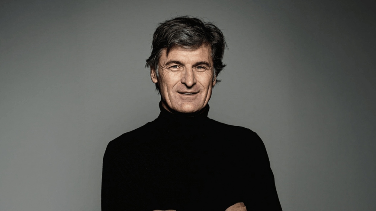 Rainer Maelzer in a black turtleneck smiling confidently with arms crossed.
