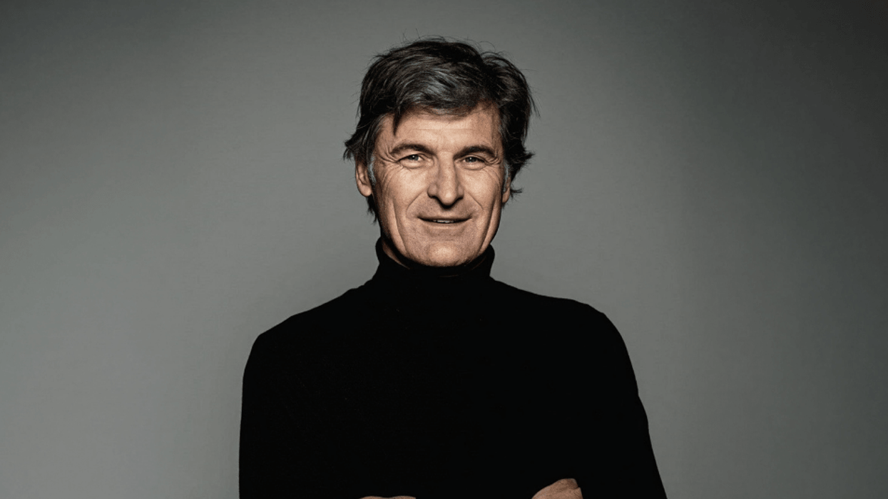 Rainer Maelzer in a black turtleneck smiling confidently with arms crossed.