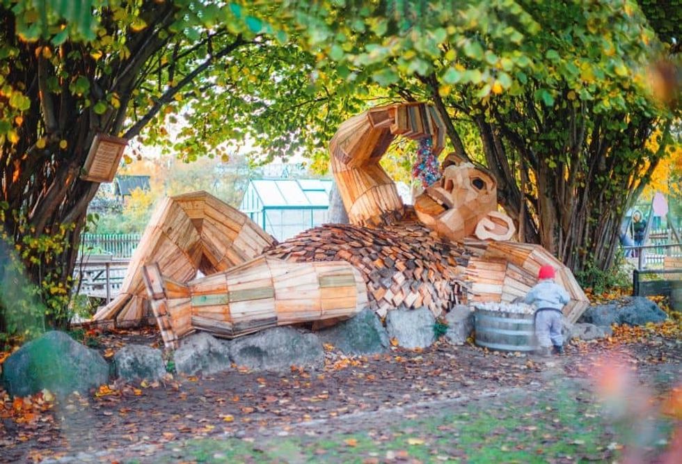 Recycled troll sculpture lying on side by trees from Imagine Exhibitions new exhibit
