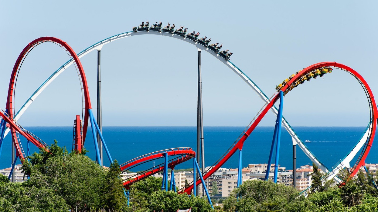 Red and blue roller coaster at PortAventura World loops with ocean and buildings in the background.