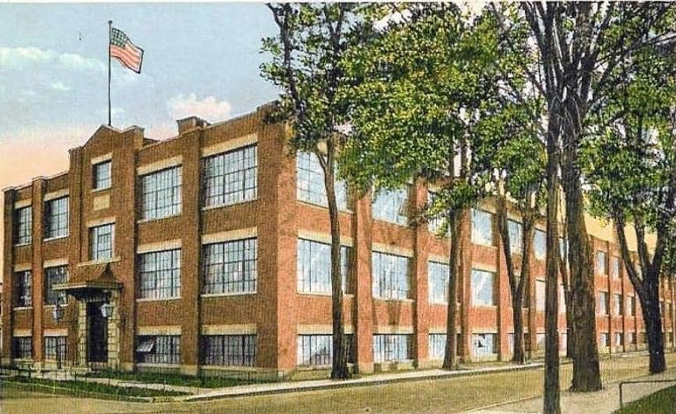 Red-brick building with large windows, tall trees, and a U.S. flag atop the roof.