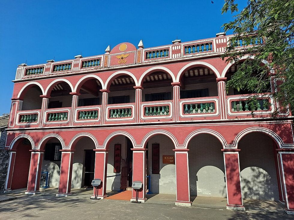 Red building with arches, green railings, and blue sky background.