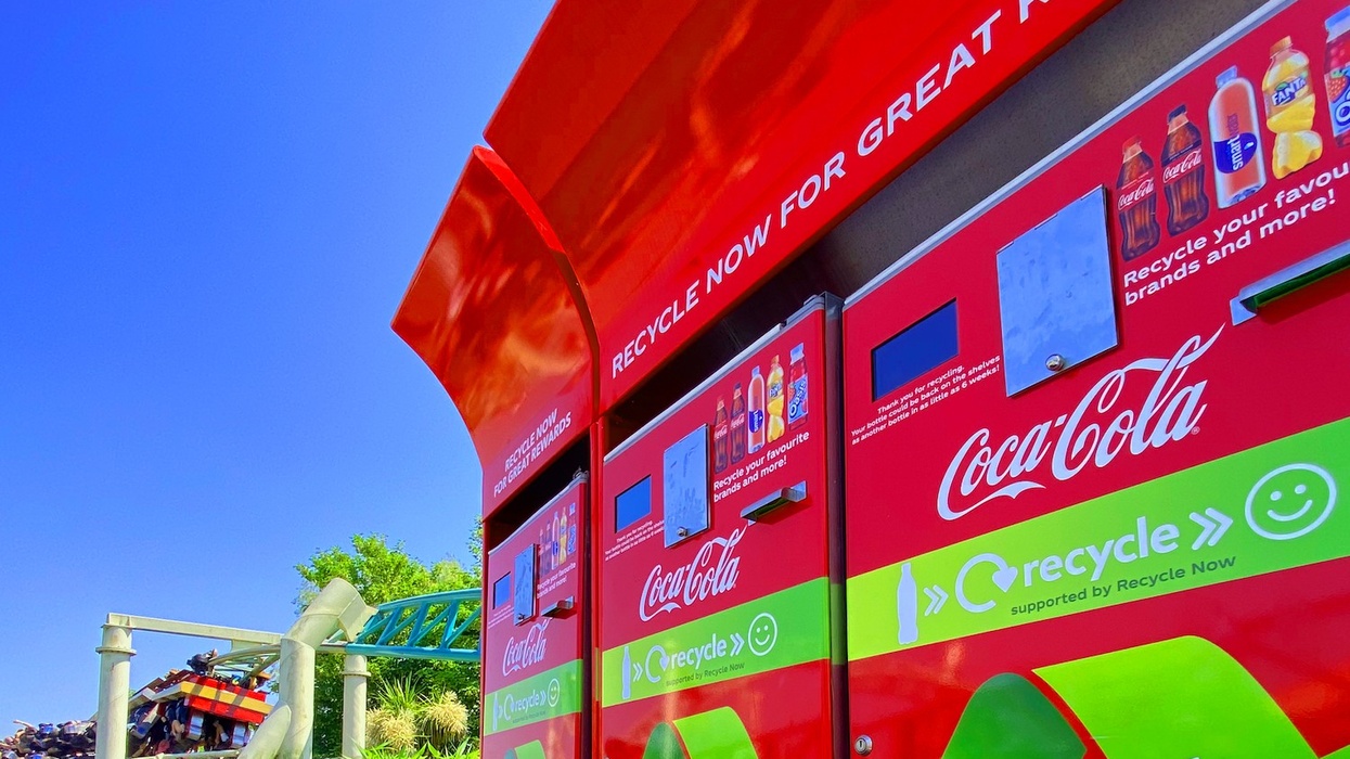 Red Coca-Cola recycling station near a roller coaster on a sunny day.