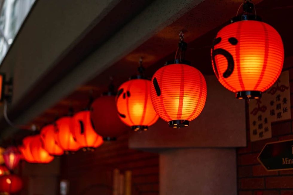 Red Japanese lanterns hanging, glowing warmly in a row under a roof.