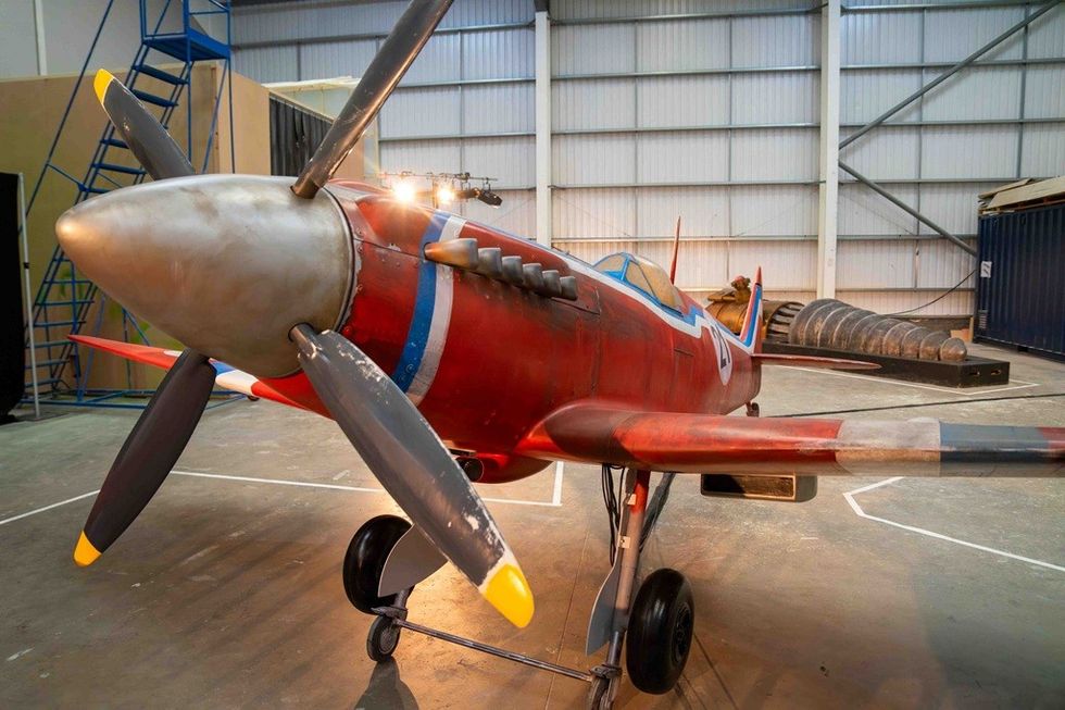 Red propeller airplane on display in a hangar with blue and white stripes.