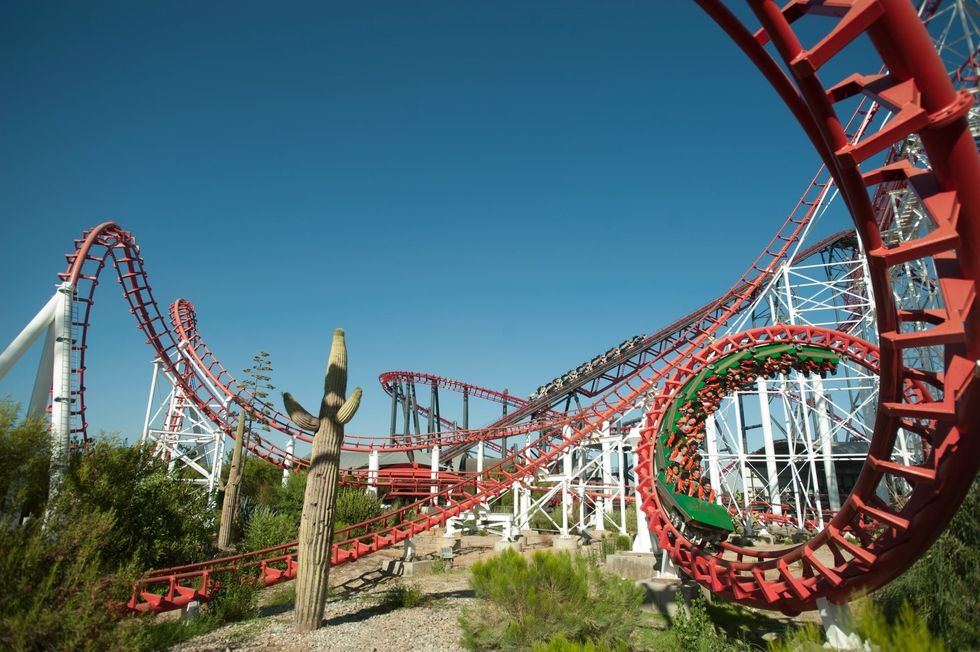 Red roller coaster with loops and cactus in foreground against clear blue sky at Six Flags Magic Mountain