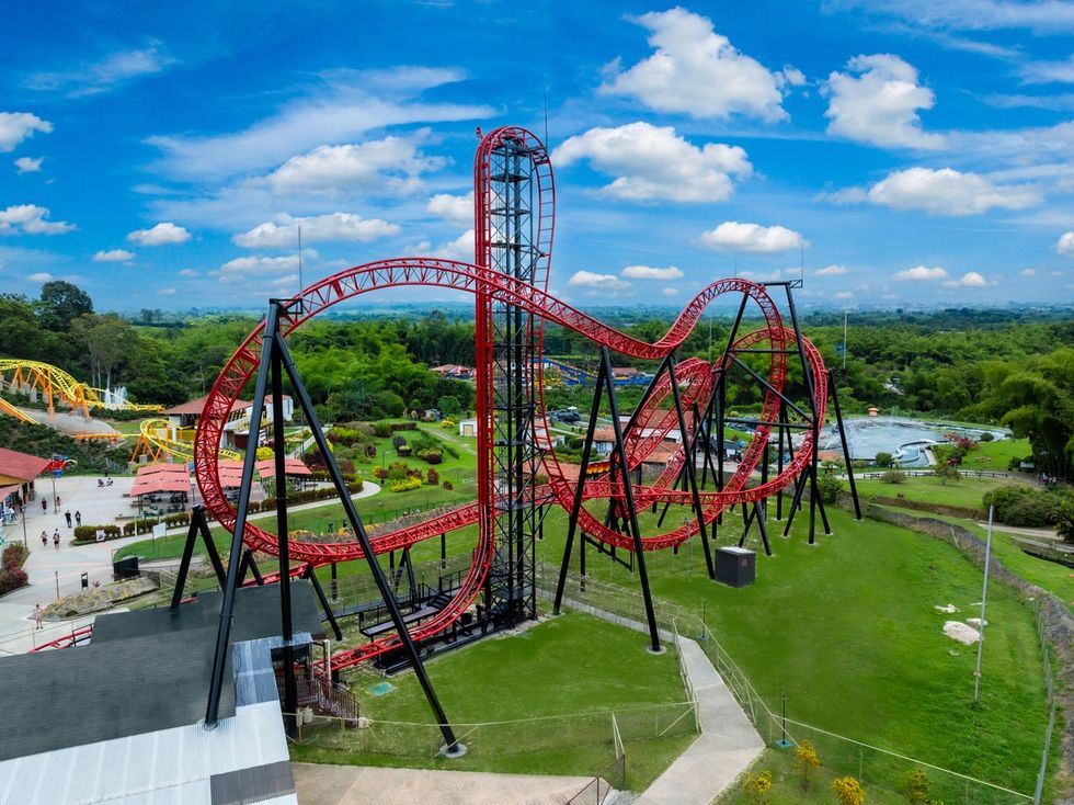 Red roller coaster with loops and twists under a blue sky in a green amusement park called Parque del Caf\u00e9