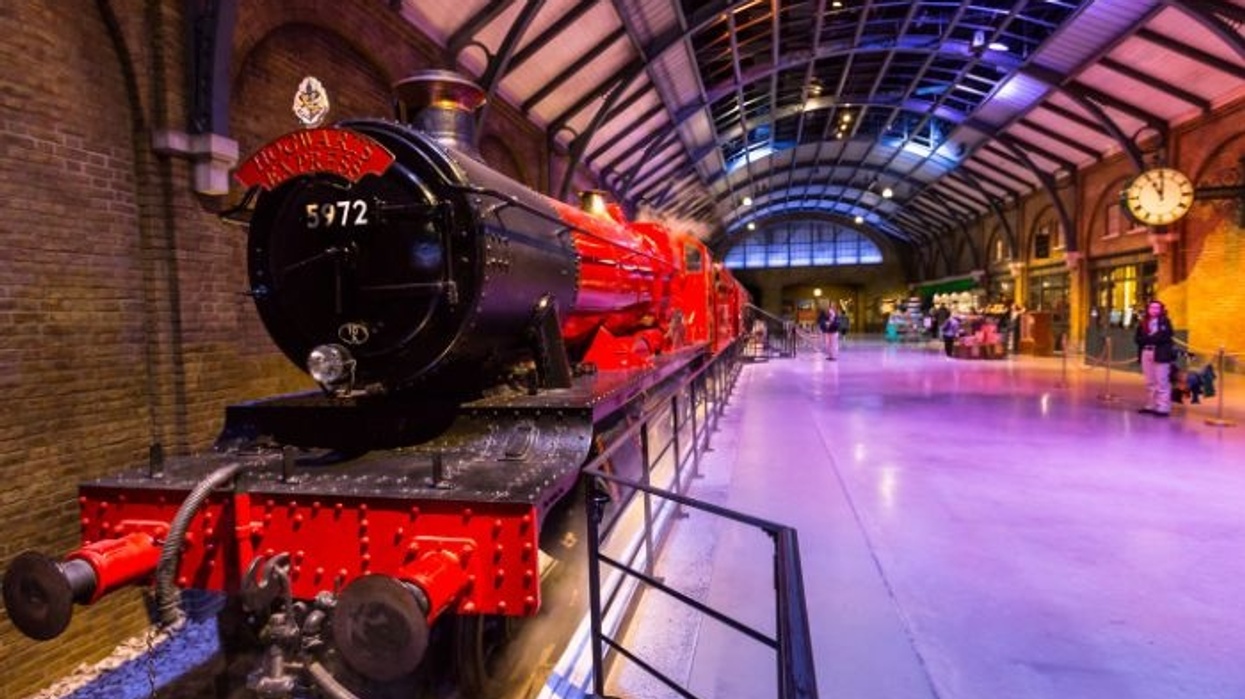 Red steam train in a spacious, arched train station with a clock on the wall.