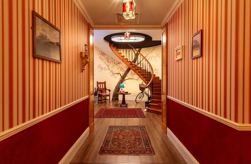 Red striped hallway with spiral staircase, tree mural, and decorative rugs.