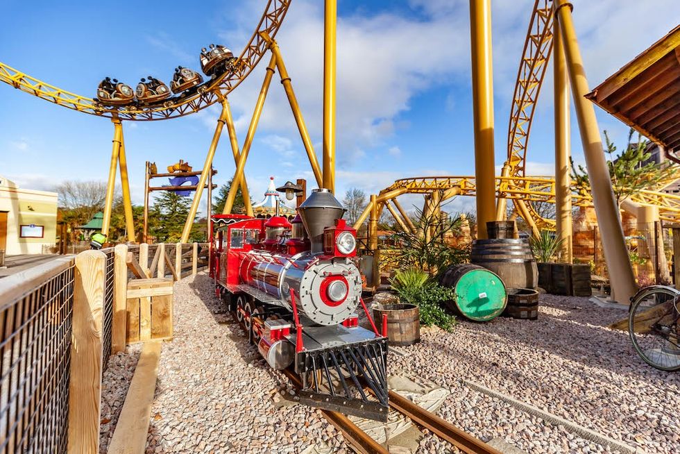 Red toy train in front of a looping rollercoaster at an amusement park, Tornado Springs at Paultons Park