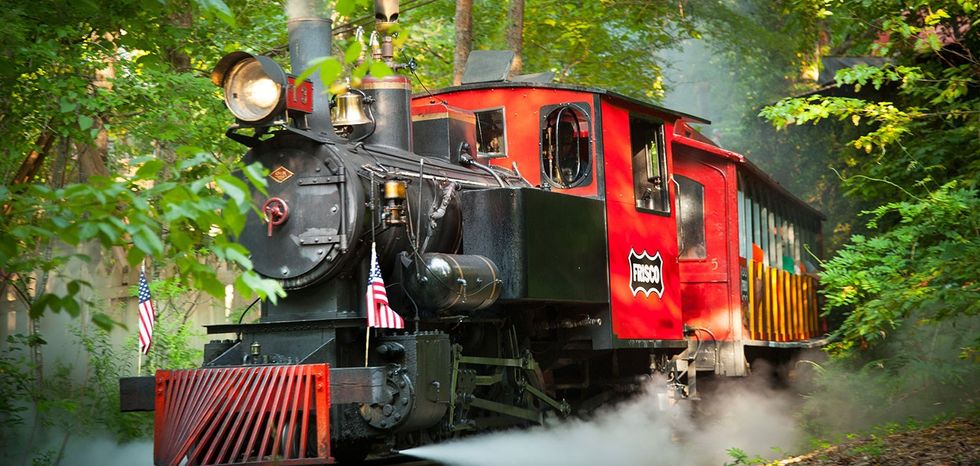 Red vintage steam train in a lush, green forest setting.