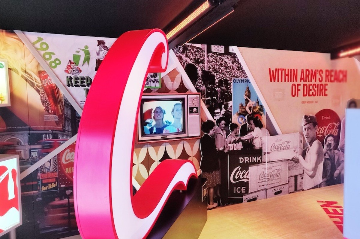 Retro Coca-Cola exhibit featuring vintage ads, a large red logo, and a small television display.