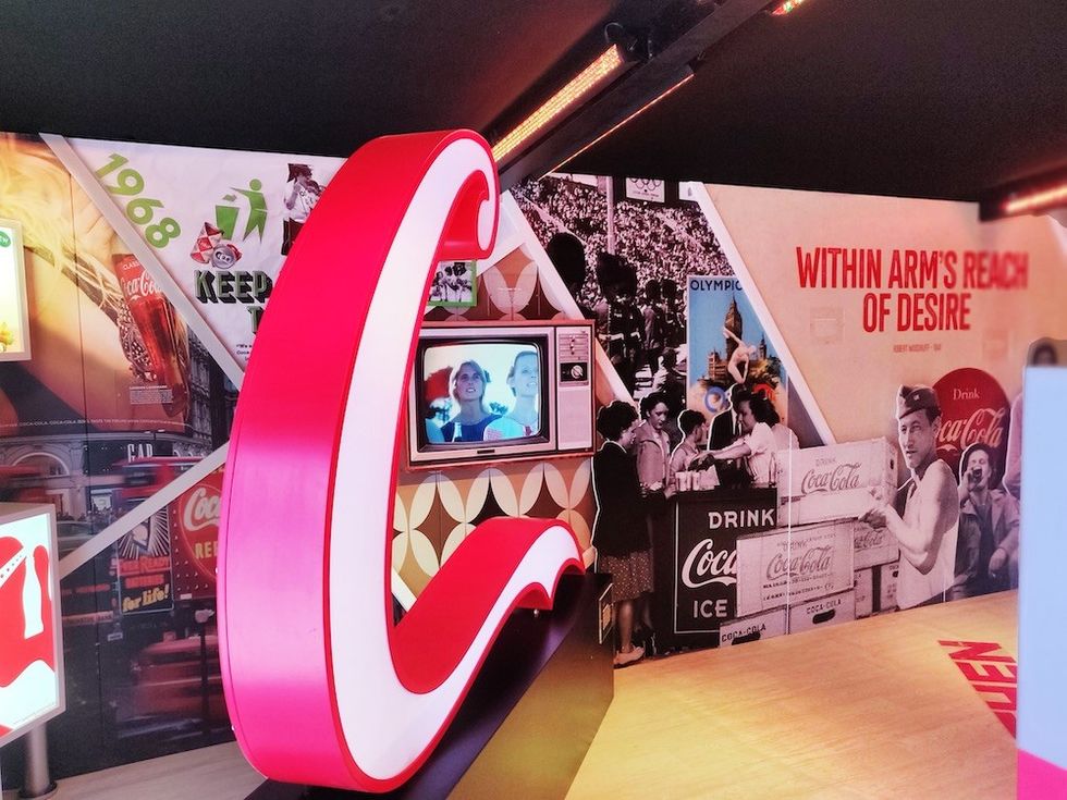 Retro Coca-Cola exhibit featuring vintage ads, a large red logo, and a small television display.