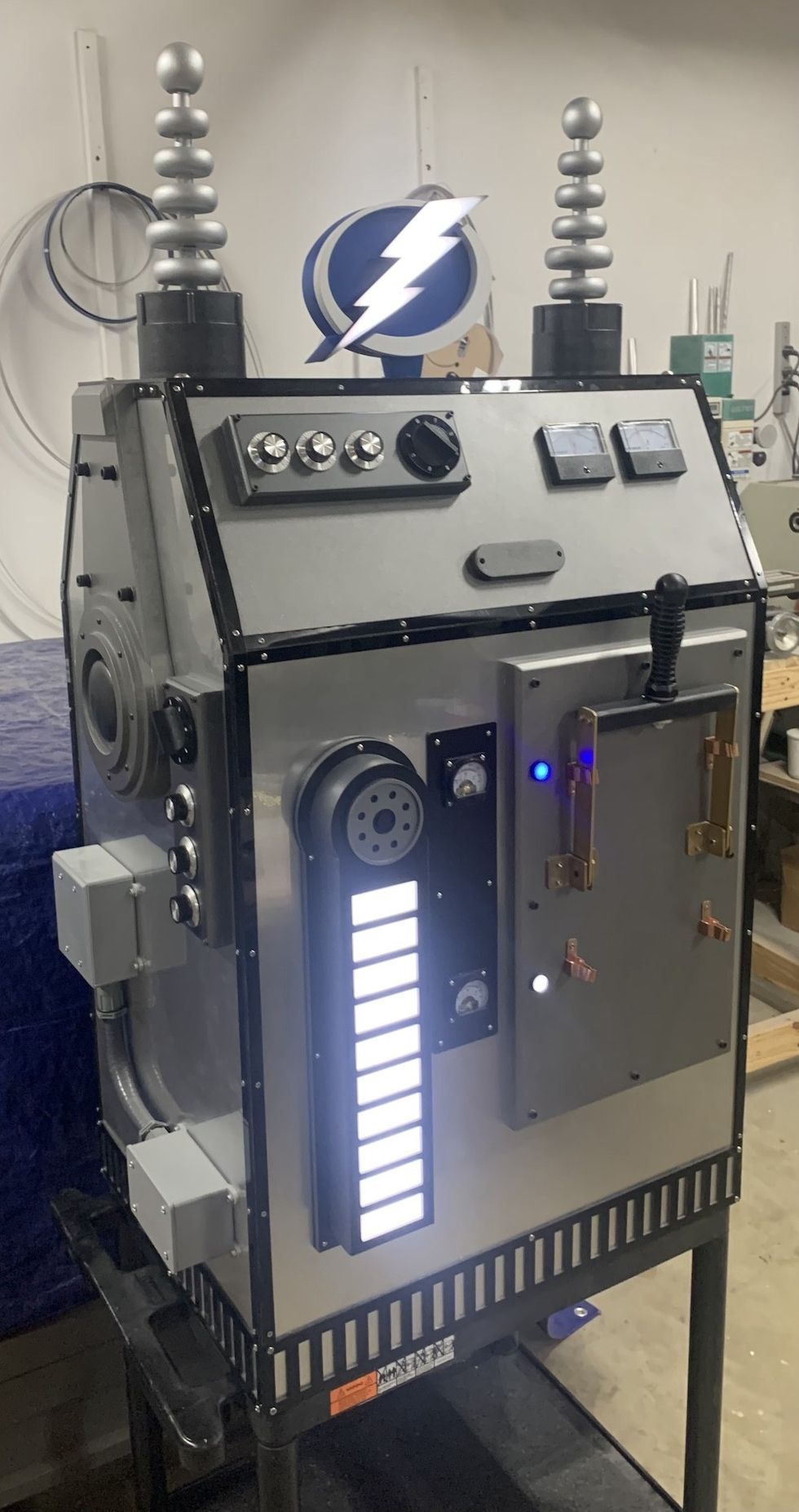 Retro sci-fi machine with dials, levers, and illuminated panels in a workshop setting.