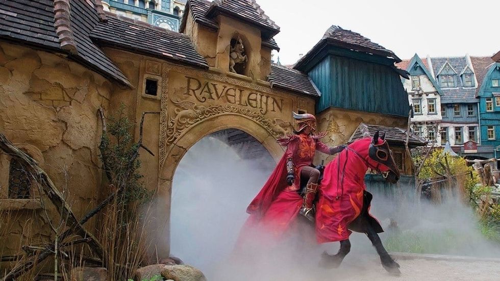 Rider in red costume on horseback emerging from a misty, medieval archway at Efteling's Ravelijn show.