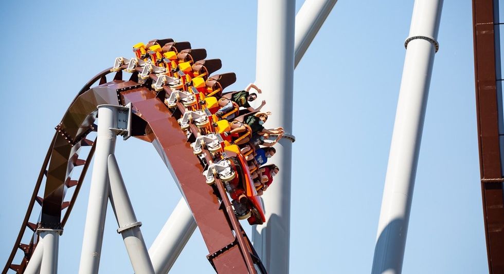 Riders descending a steep roller coaster with arms raised against a blue sky.
