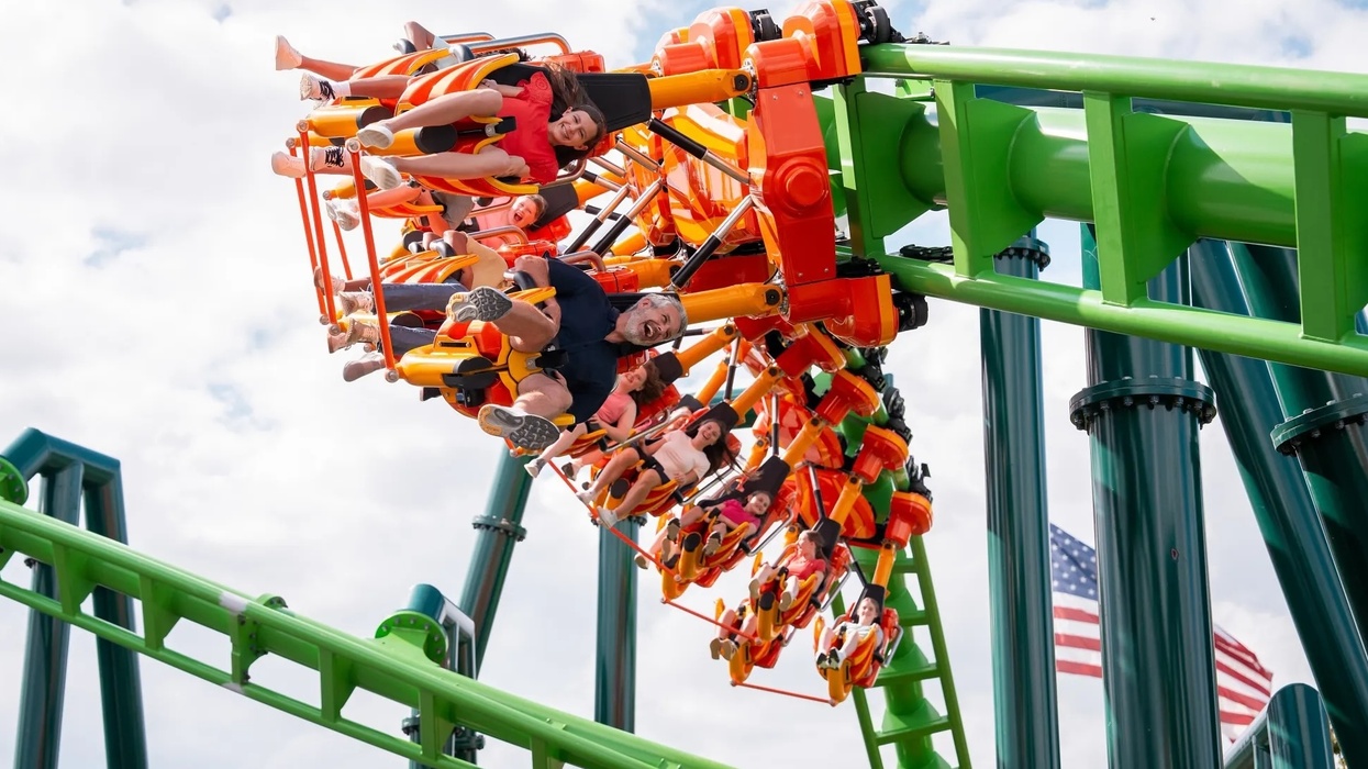 Riders on a colorful upside-down roller coaster called Flying Fox at Kentucky Kingdom with an American flag in the background.