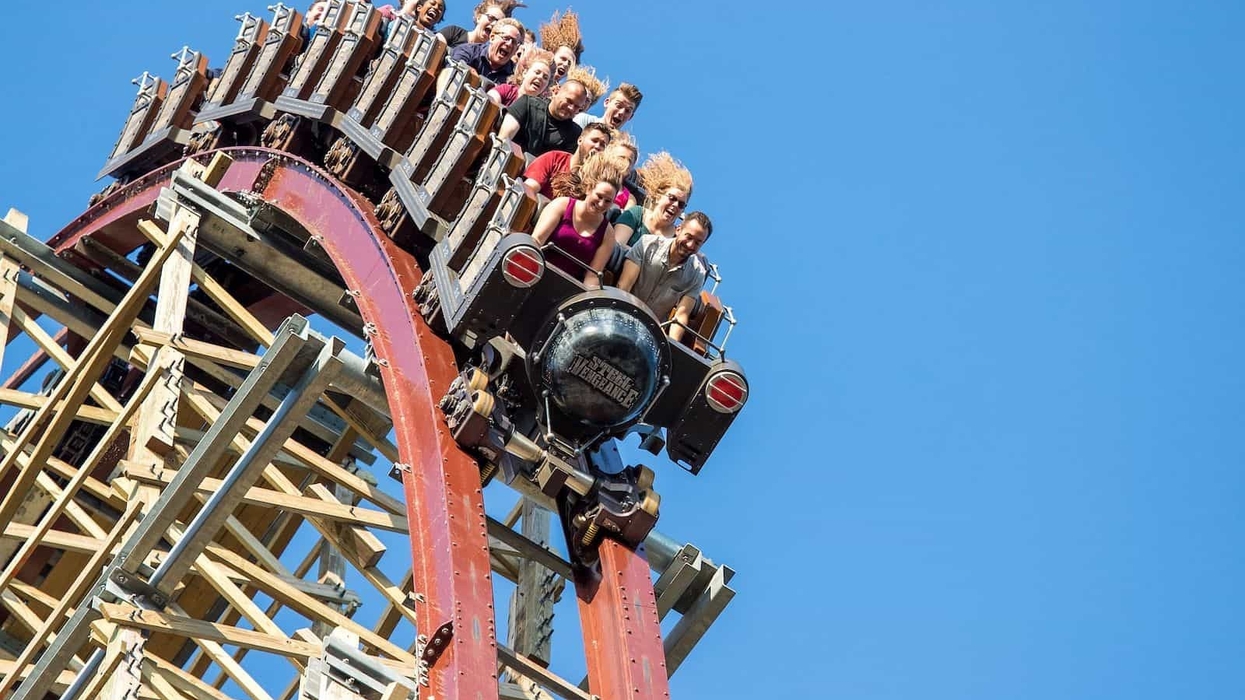 Riders on a steep wooden roller coaster drop under a clear blue sky at Cedar Point