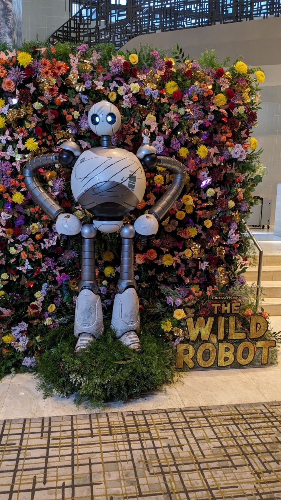 Robot statue in front of a colorful floral wall display.