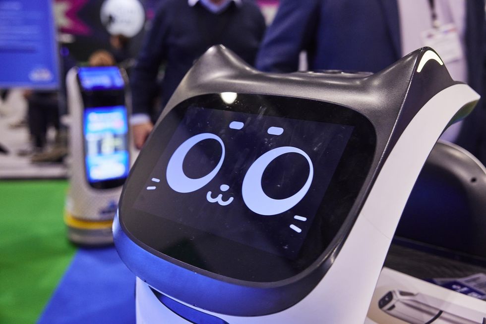 Robotic device with a cat face display at a tech expo, people in background.