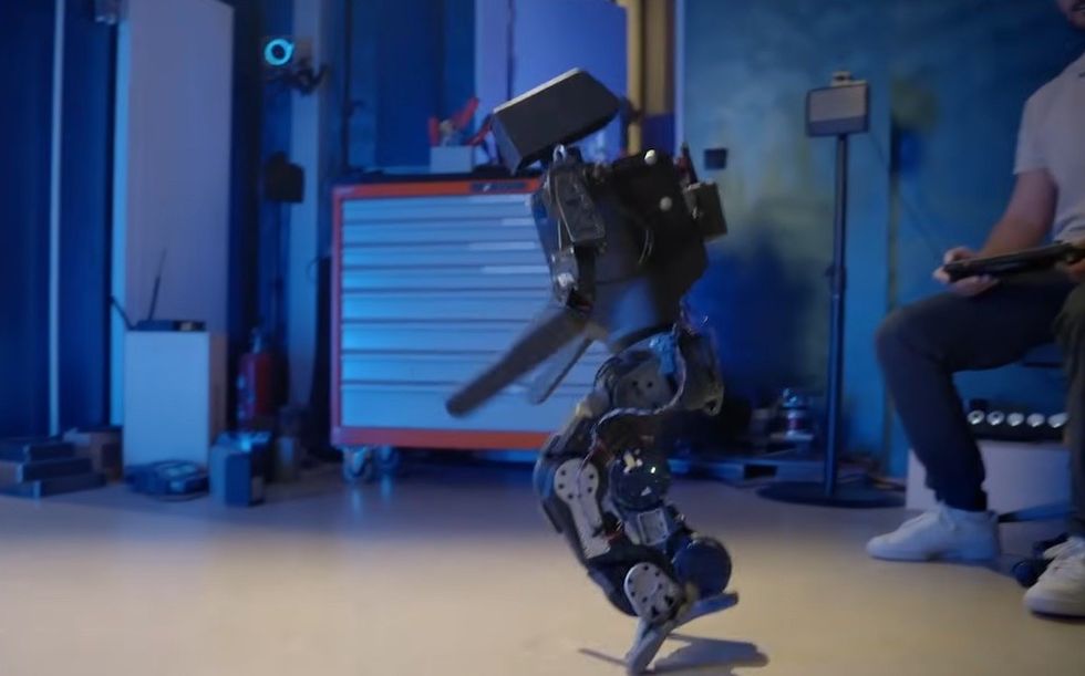 Robotic figure in a tech lab with a person controlling it nearby.