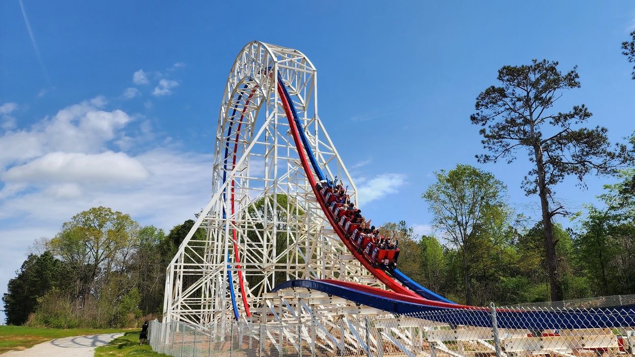 Roller coaster ascending steep track with riders, set against a clear blue sky