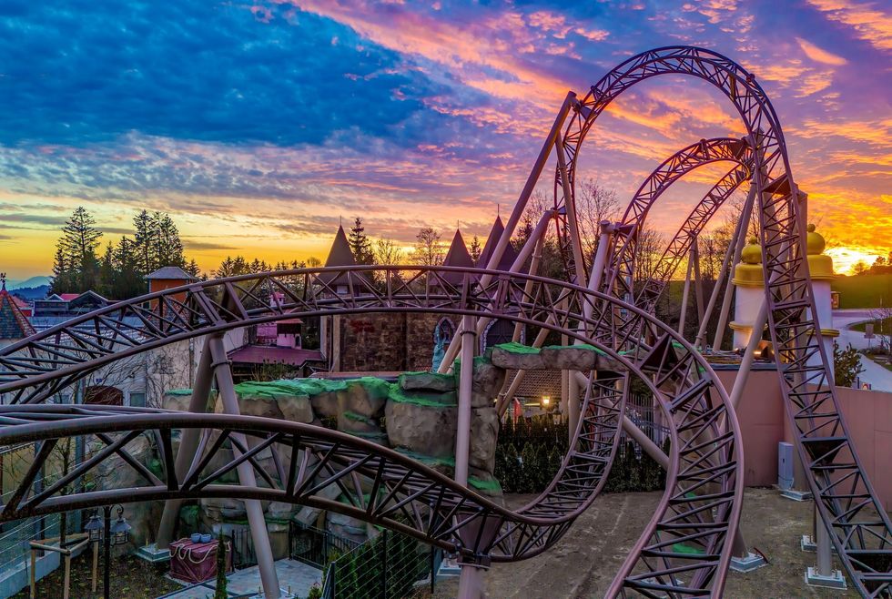 Roller coaster at sunset with vibrant sky and lush trees in the background.