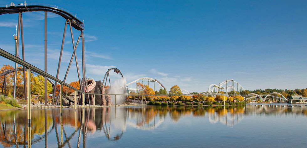 Roller coaster beside a lake with a blue sky and autumn trees.