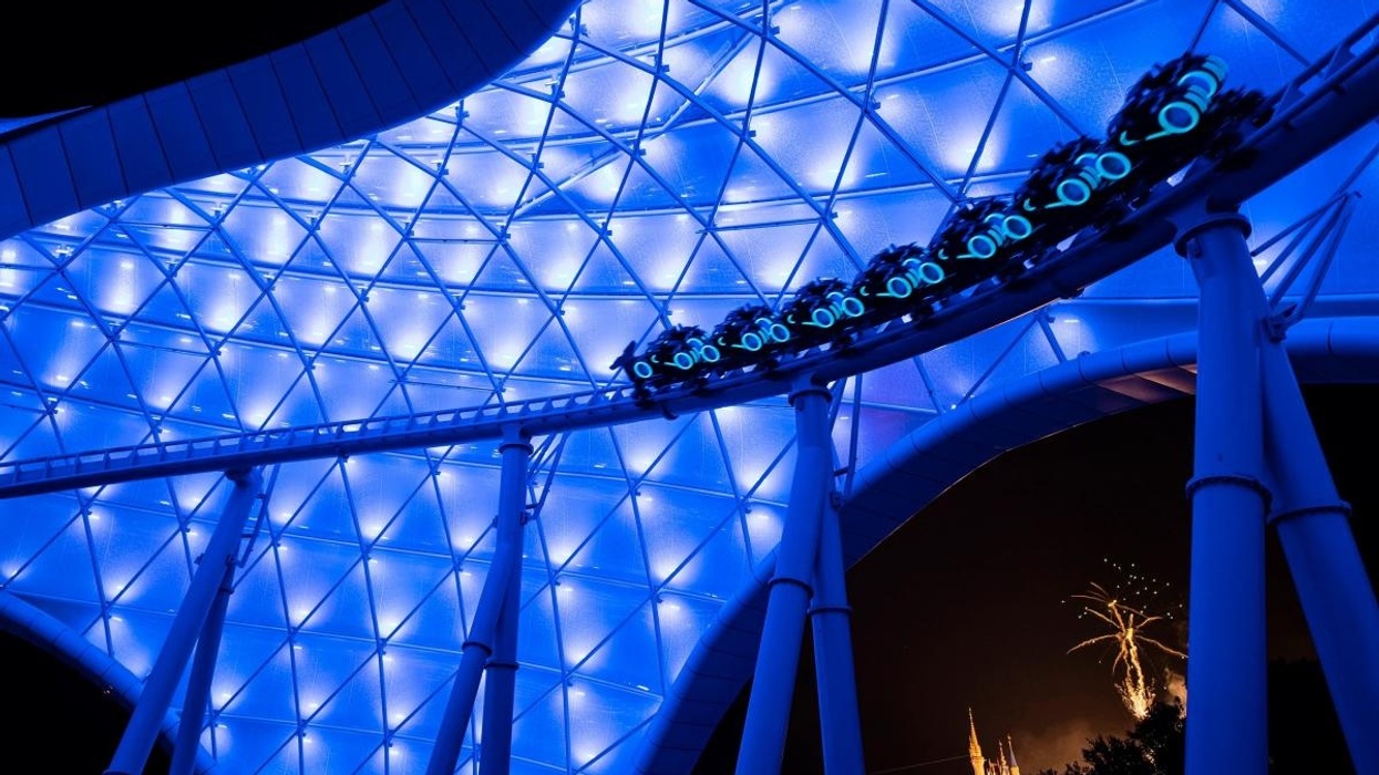 Roller coaster called TRON Lightcycle / Run under glowing blue canopy with fireworks in the background.