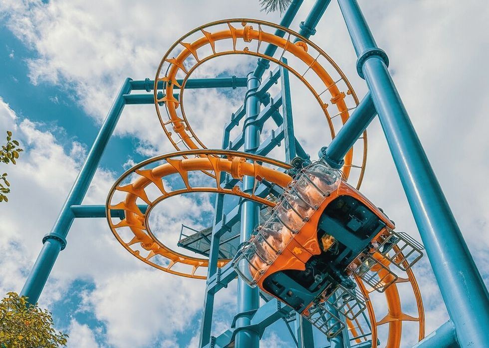 Roller coaster car upside-down on a loop against a cloudy blue sky.