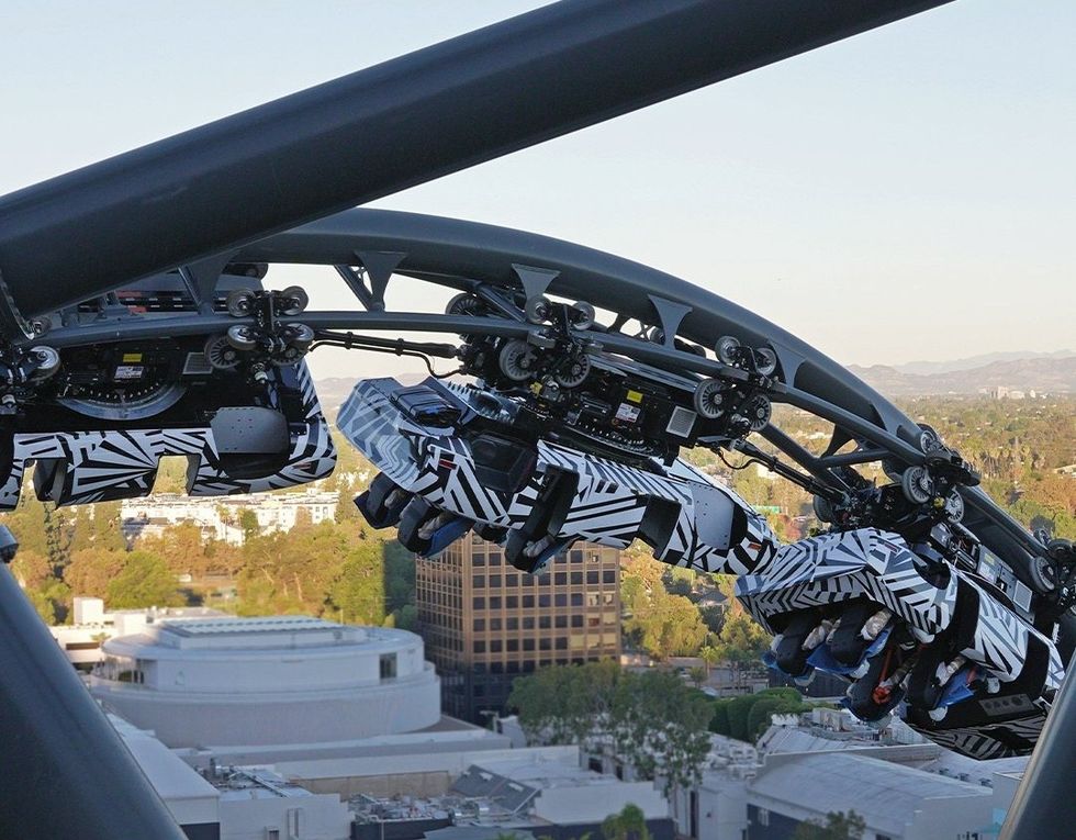 Roller coaster cars on Fast & Furious coaster at Universal Hollywood, upside down on a loop, with a cityscape in the background.