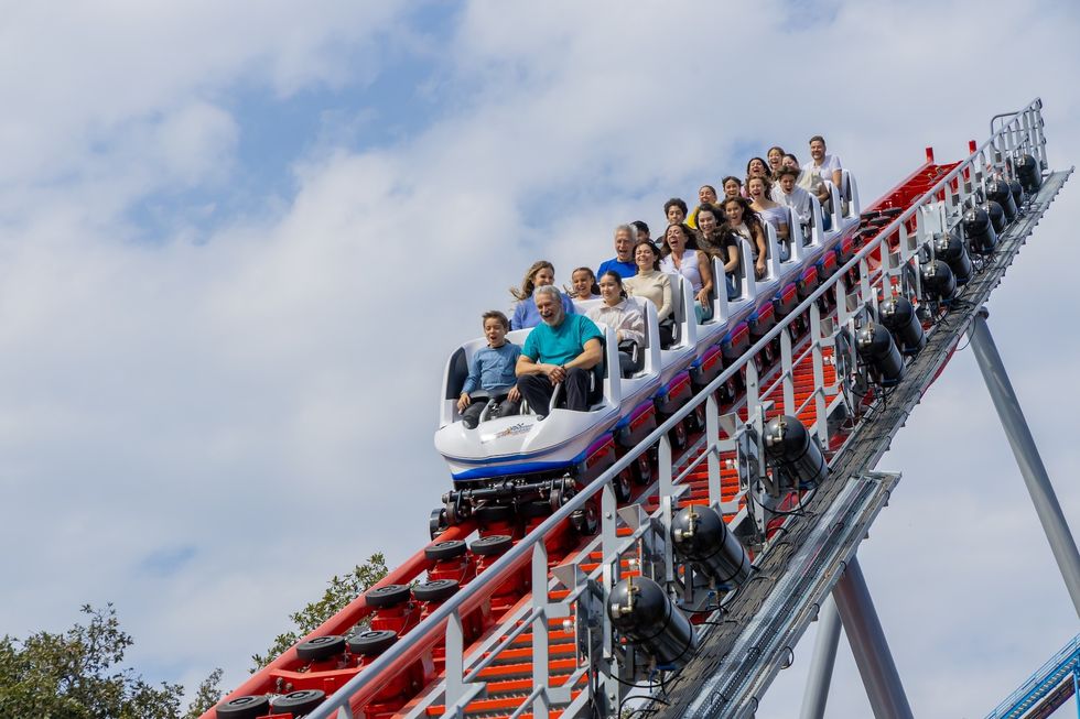 Roller coaster descending with excited riders under a blue sky at Six Flags Mexico