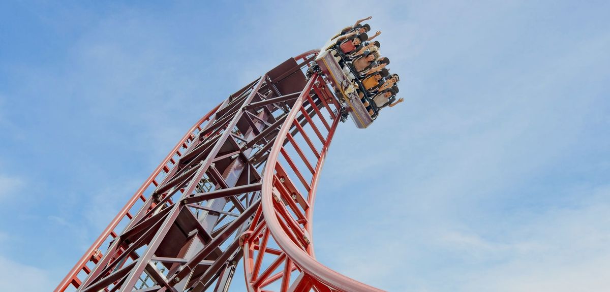 Roller coaster, Drakon at Paultons Park, ascending steep track with people raising their hands under a clear blue sky.