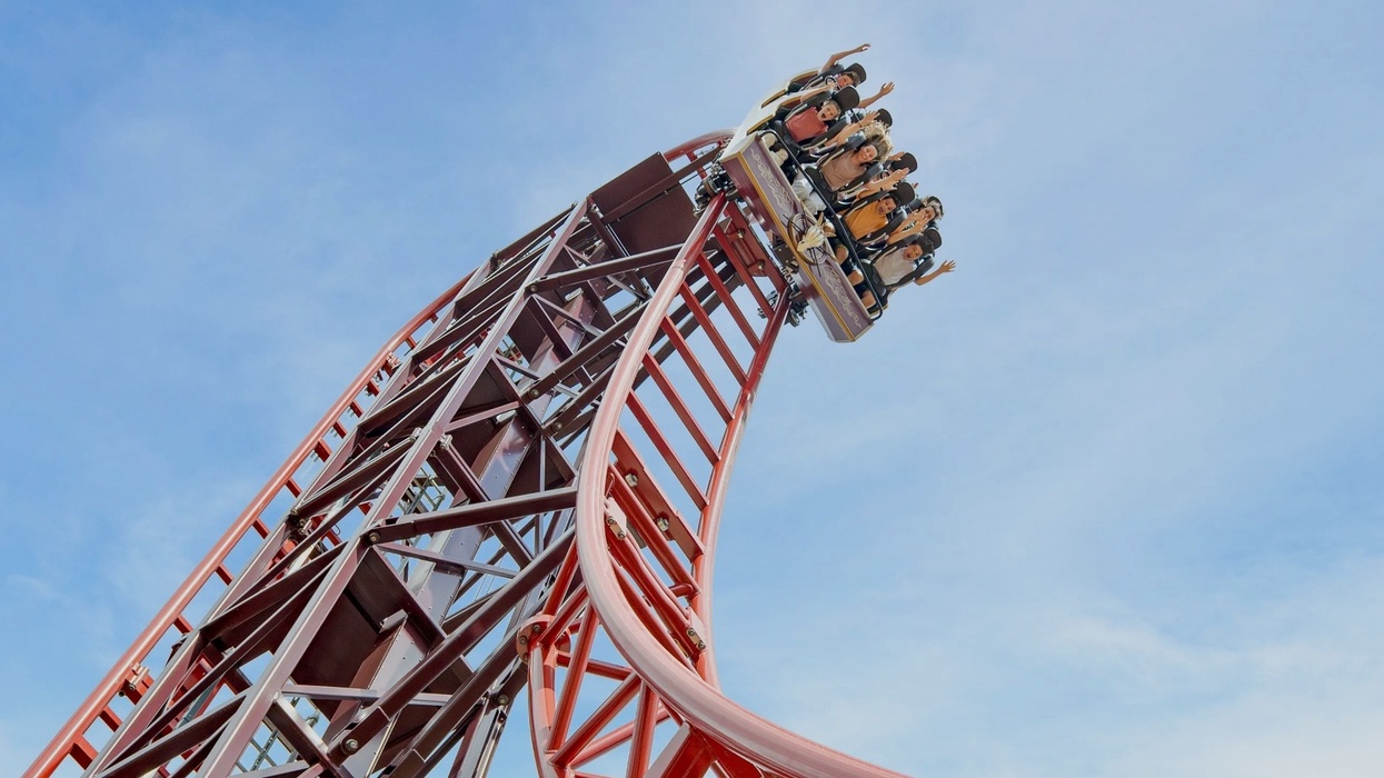 Roller coaster, Drakon at Paultons Park, ascending steep track with people raising their hands under a clear blue sky.