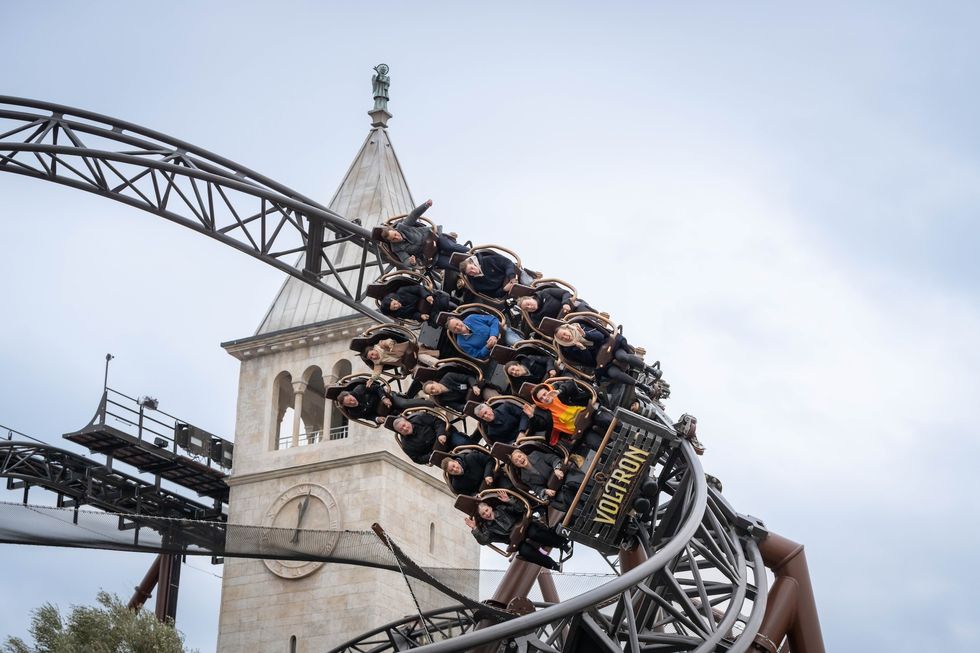 Roller coaster full of passengers upside down near clock tower at Europa-Park