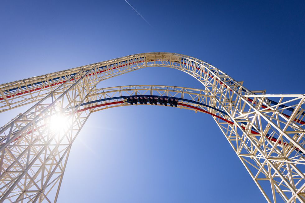 Roller coaster loop against clear blue sky with bright sunlight.
