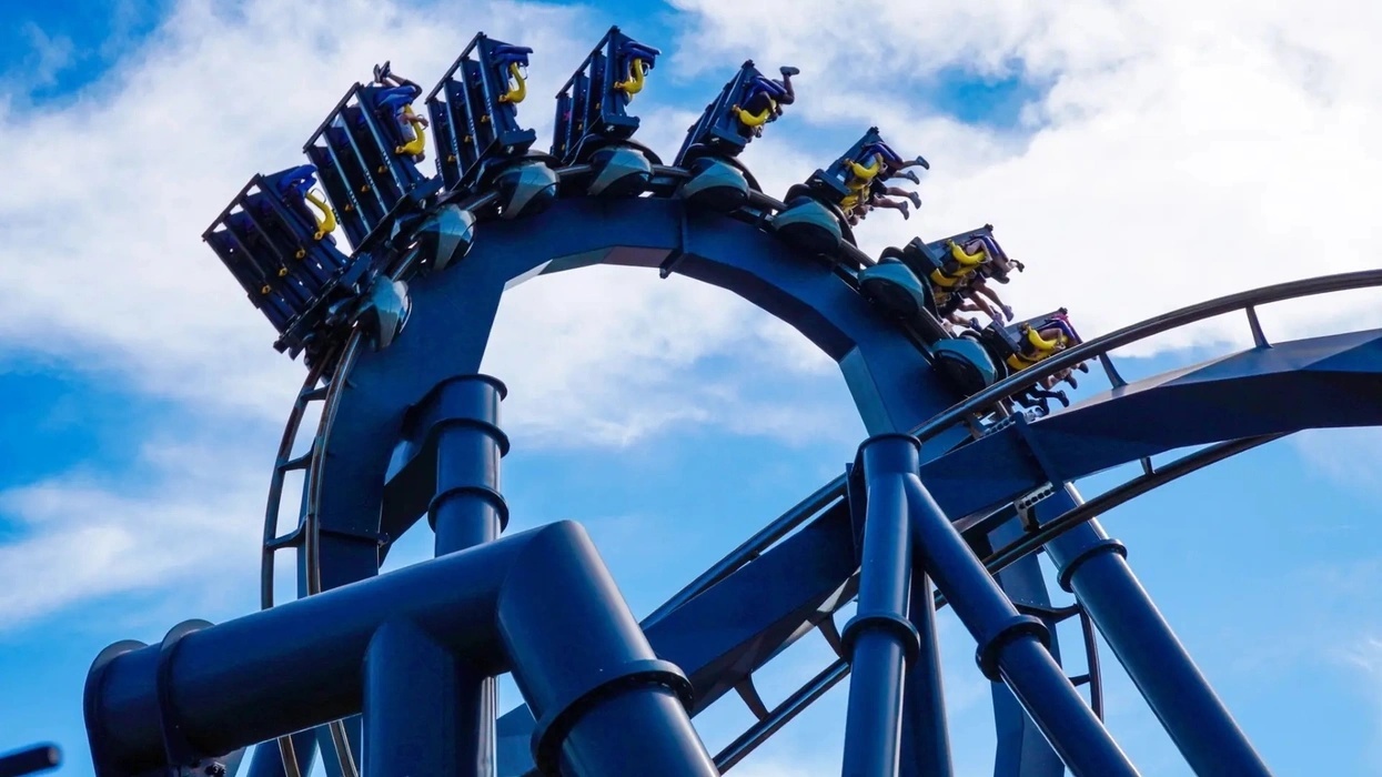 Roller coaster loop with riders against a bright blue sky and clouds at Mid America Adventure