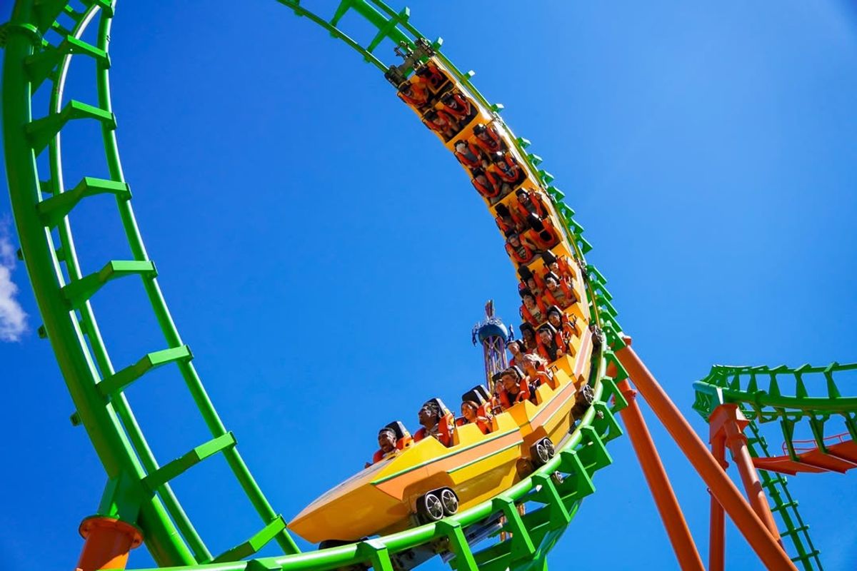 Roller coaster loop with riders against a clear blue sky at Six Flags