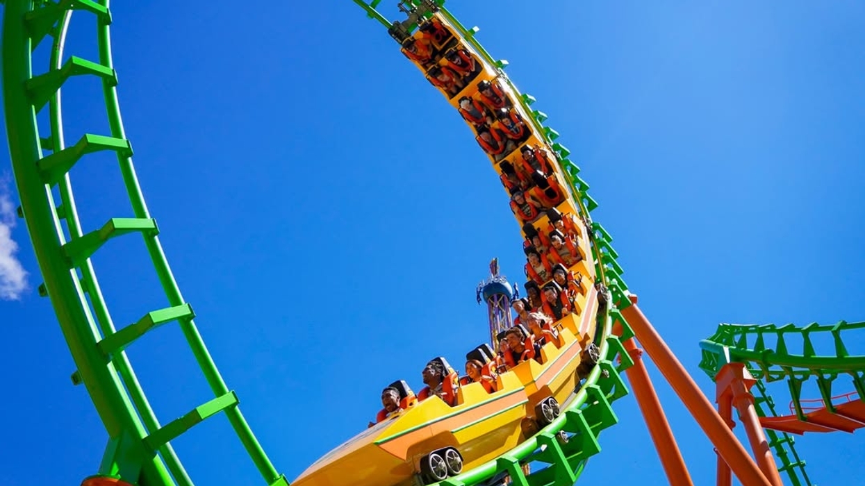 Roller coaster loop with riders against a clear blue sky at Six Flags
