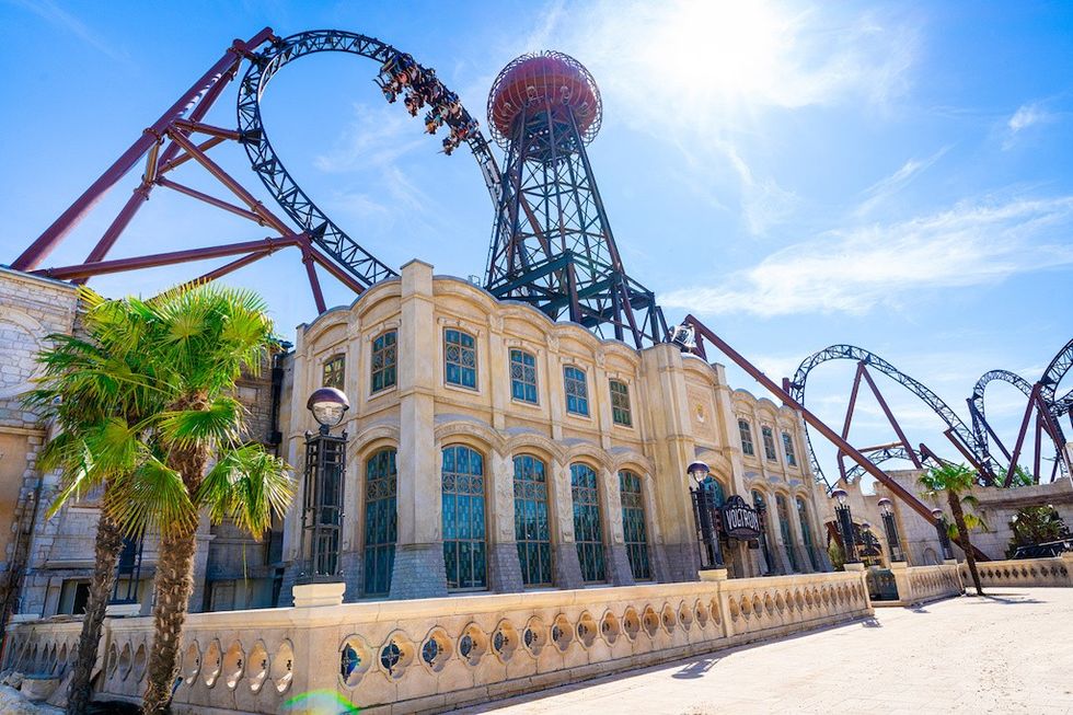Roller coaster loops around ornate building under a sunny blue sky.