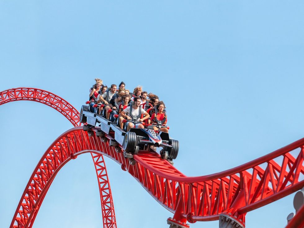Roller coaster ride with excited passengers on a red track under a clear blue sky