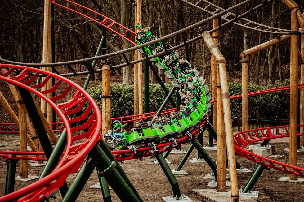 Roller coaster ride with people in bright green cars on a wooden and metal track.
