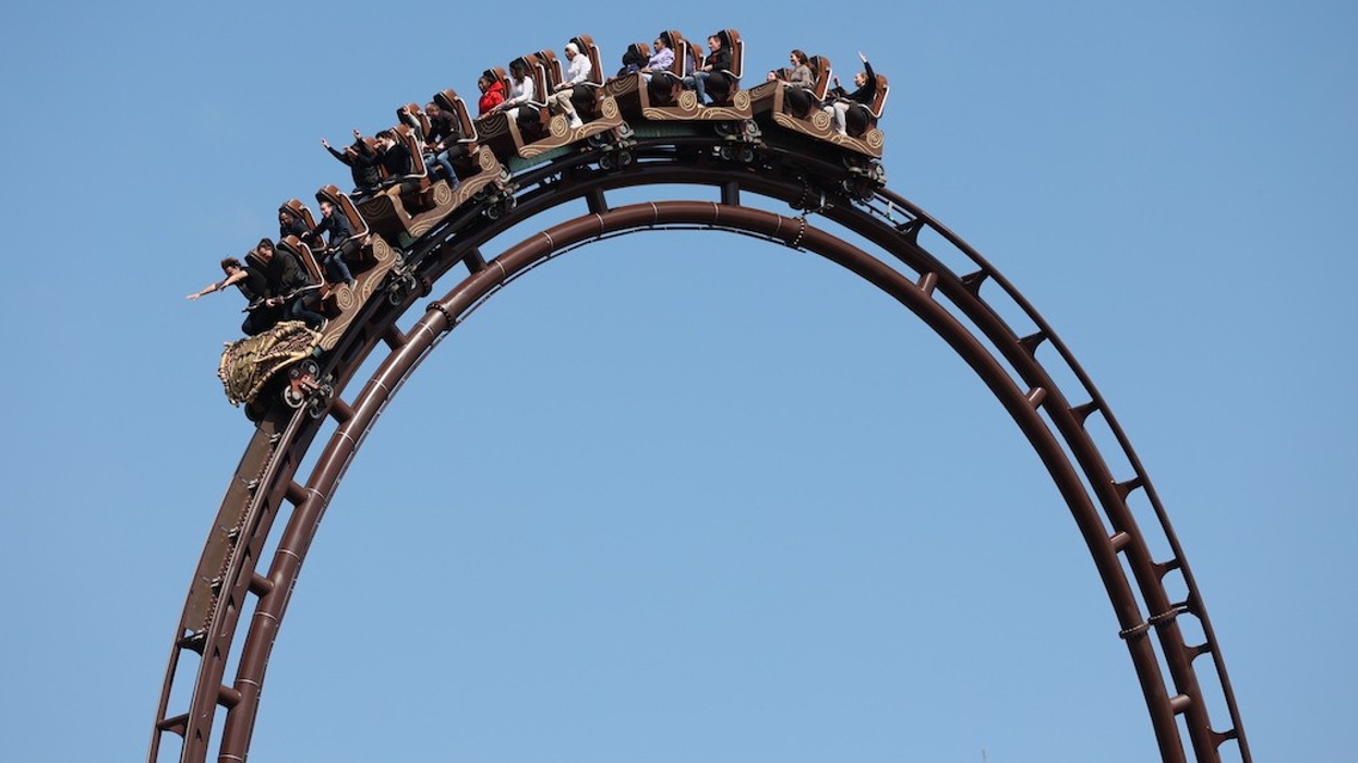 Roller coaster riders descend a steep loop against a clear blue sky, on Toutatis at Parc Astérix
